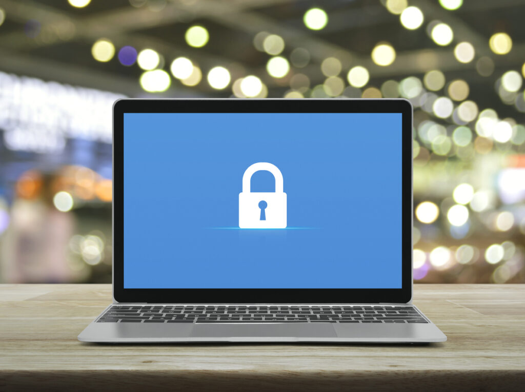 Padlock icon on modern laptop computer monitor screen on wooden table over blur light and shadow of shopping mall, Technology internet cyber security and safety online concept